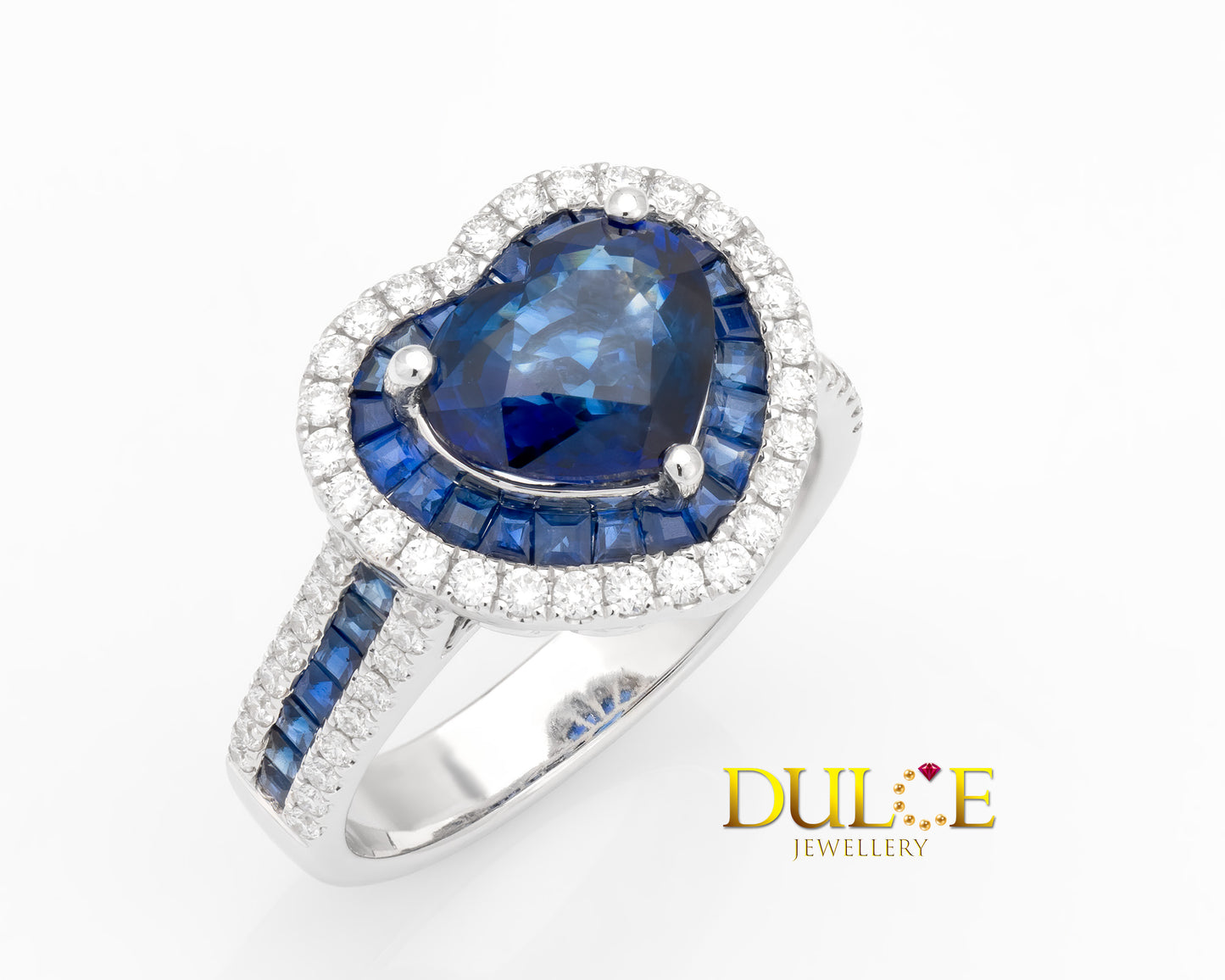 "Heart-shaped royal blue sapphire surrounded by a halo of small blue sapphires and sparkling diamonds in a polished gold setting."